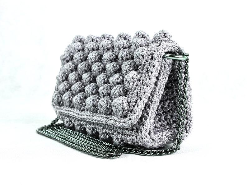 May include: A gray crocheted handbag with a silver chain strap. The bag has a textured, puffy design.