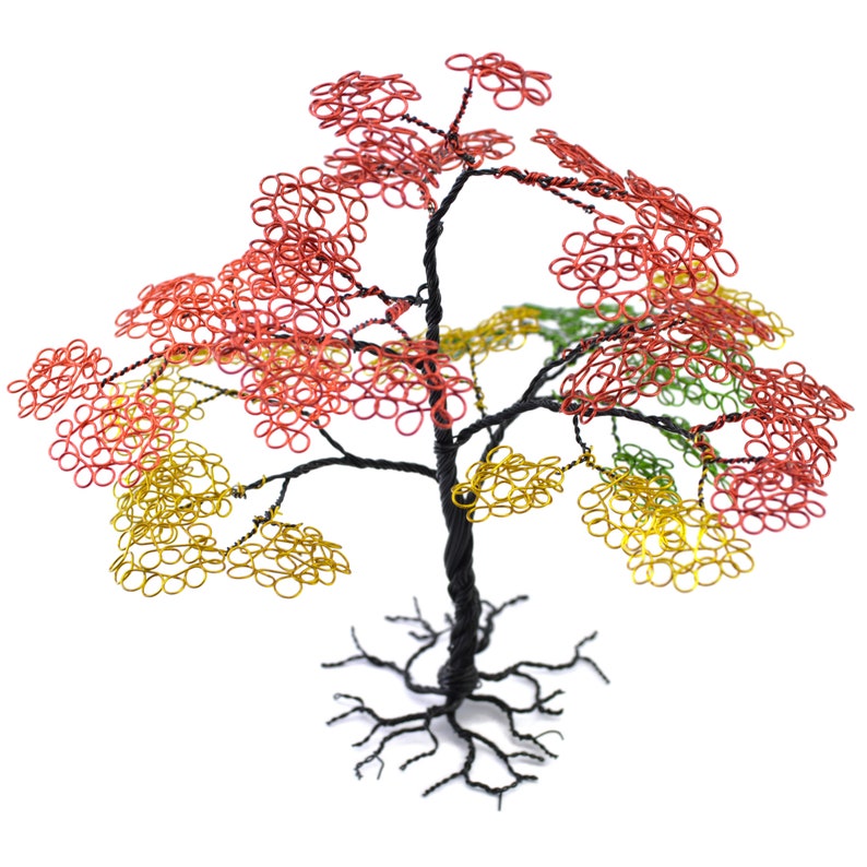 Pu&ograve; includere: Scultura di albero in filo di ferro fatta a mano con un tronco e radici neri. Il fogliame dell'albero presenta anelli di filo rosso, giallo e verde, creando una rappresentazione artistica e colorata di un albero. Su sfondo bianco.