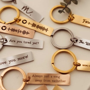 K&ouml;nnte beinhalten: Eine Sammlung von Schl&uuml;sselanh&auml;ngern aus Silber, Gold und Ros&eacute;gold mit gravierten Botschaften. Die Schl&uuml;sselanh&auml;nger zeigen verschiedene Botschaften, darunter "Forever", "The Wonder of You", "Are you tired yet?", "Love you more!", "Always just a song away from each other" und "Bring on your wreck".