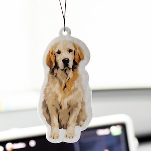 May include: A hanging air freshener shaped like a golden retriever dog. The illustration features the dog in a seated position with light golden and cream-coloured fur, dark brown eyes, and a black nose. A thin black elastic string is attached to the top.