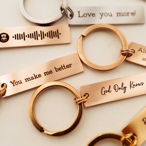 K&ouml;nnte beinhalten: Ein Satz Schl&uuml;sselanh&auml;nger aus Gold und Silber mit gravierten Botschaften. Die Botschaften lauten "You make me better", "Love you more", "Always just away from", "God Only Knows" und ein Barcode mit einem kleinen B&auml;ren-Symbol.
