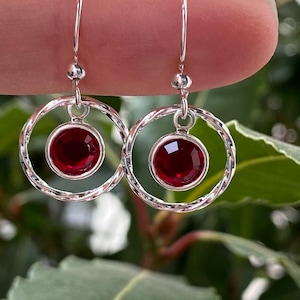 May include: Silver dangle earrings with a red gemstone in a circle setting.