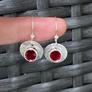 May include: A pair of silver dangle earrings with a textured round disc and a red gemstone in the centre.