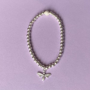 May include: Silver beaded bracelet with a bee charm. The bracelet is made of small, round silver beads, with a textured silver bead at the top. A detailed bee charm hangs from the centre, adding a touch of nature-inspired elegance.