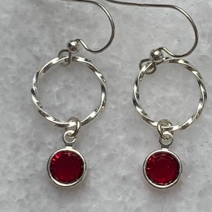May include: A pair of silver earrings with a twisted hoop design and a dangling red gemstone.
