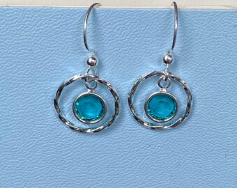 May include: Silver dangle earrings with a turquoise blue gemstone in a circle setting.