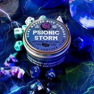 May include: A silver candle tin with a blue label that reads "Game Master Dice Company" and "Psionic Storm". The candle is 100% natural soy wax and is handmade in the USA. The label also includes the text "Audentis Fortuna Juvat" and "Cloudburst of Green Leaves, Rose Petals, and Rain Water".