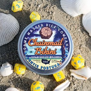 May include: A silver tin candle with a blue and yellow label that reads "Game Master Dice Company" and "Chainmail Bikini". The candle is surrounded by seashells and dice.