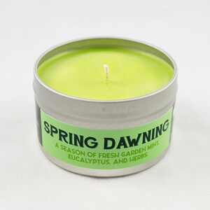 May include: A green candle in a silver tin with the text "Spring Dawning. A season of fresh garden mint, eucalyptus, and herbs."