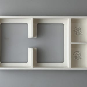 May include: White plastic tray with two rectangular compartments and two smaller compartments with a geometric design.
