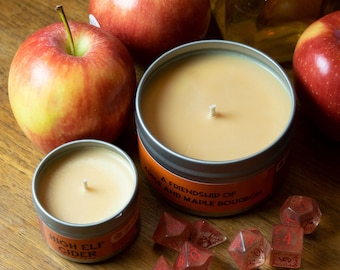 May include: Two candles in glass jars with lids, one labeled "High Elf Cider" and the other "Add a Friendship of Wine and Maple Bourbon".  The candles are surrounded by red apples and dice.