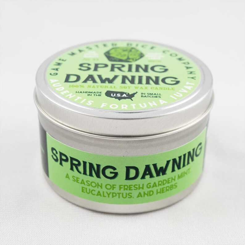May include: A silver tin candle with a green label that reads "Spring Dawning 100% Natural Soy Wax Candle" and "A season of fresh garden mint, eucalyptus, and herbs".