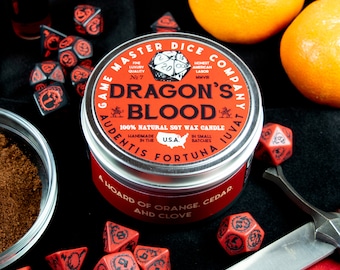 May include: A silver tin candle with a red and black label that reads "Game Master Dice Company" and "Dragon's Blood". The candle is 100% natural soy wax and is handmade in the USA. The label also includes the text "Audentis Fortuna Juvat" and "A Hoard of Orange, Cedar and Clove".