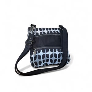 May include: A black and white patterned crossbody bag with a black adjustable strap. The bag has three zipped compartments and silver-toned hardware. The pattern is a repeating design of white and grey shapes.