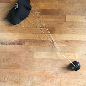 Può includere: Un calzino nero con un disegno bianco è attaccato a un piccolo peso nero da una lunga corda, creando un paracadute improvvisato.