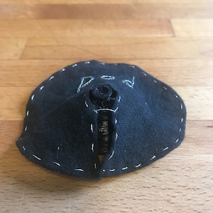 May include: Black fabric circle with a white stitched edge and a black button in the centre.