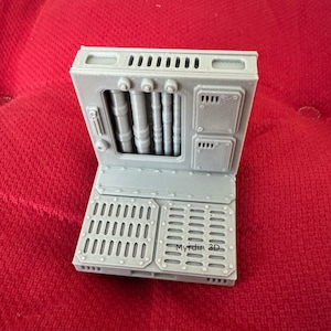 May include: A gray 3D printed model of a wall panel with a grated floor and a panel with pipes and vents. The panel has the text "Myrdin 3D" printed on it.