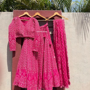 May include: A pink embroidered three-piece outfit with a long-sleeved blouse, a skirt, and a dupatta. The outfit is decorated with silver sequins and beads. The text "Radha Fashion Boutique" is visible on the skirt.