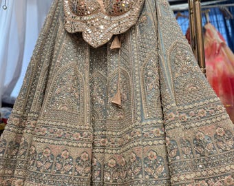 May include: A formal, embellished ensemble featuring a light blue skirt and a matching top. The top is adorned with reflective embellishments. The skirt showcases intricate embroidery and floral patterns, creating a luxurious and detailed appearance. The outfit is displayed on a hanger.