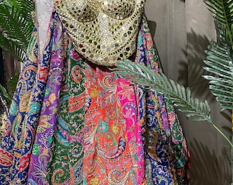 May include: A gold-colored, mirrored bodice top hangs above a vibrant, patchwork skirt. The skirt features a paisley pattern in shades of blue, green, purple, orange, and pink. The outfit is displayed on a yellow hanger against a neutral background.