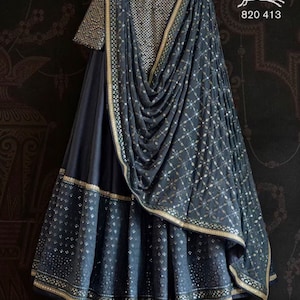 May include: A dark blue embroidered skirt with a matching dupatta, featuring silver and gold embellishments. The skirt has a layered design with a gold trim. The dupatta is draped over the skirt and has a diamond pattern. The image includes the text "Swati Manish" and "820 413".