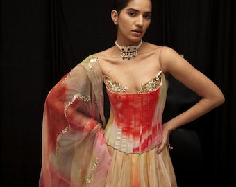 May include: A formal gown featuring a red and white bodice with gold embellishments. The dress has a flowing skirt in shades of peach and yellow. A sheer, patterned shawl and a jeweled choker complete the look.