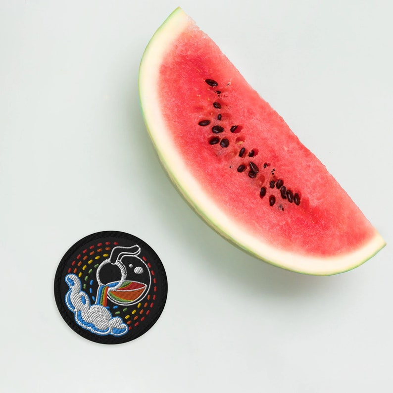 K&ouml;nnte beinhalten: Ein gestickter Patch in Schwarzwei&szlig; mit einem Regenbogen und einer Teekanne, die eine Fl&uuml;ssigkeit ausgie&szlig;t. Der Patch befindet sich auf einem wei&szlig;en Hintergrund neben einer Wassermelonen-Scheibe.