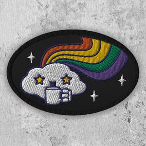 May include: A black embroidered patch with a white cloud holding a coffee cup. The cloud has two yellow stars for eyes and a rainbow is behind it. There are also small white stars scattered around the cloud.