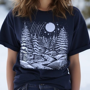 May include: A navy blue t-shirt with a white graphic print of a snowy forest scene with a full moon and shooting stars.