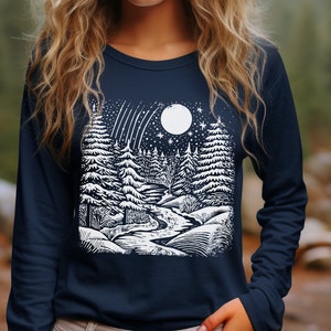 Peut inclure: Un t-shirt &agrave; manches longues bleu marine avec un imprim&eacute; graphique blanc repr&eacute;sentant une sc&egrave;ne de for&ecirc;t enneig&eacute;e avec une pleine lune et des &eacute;toiles filantes.