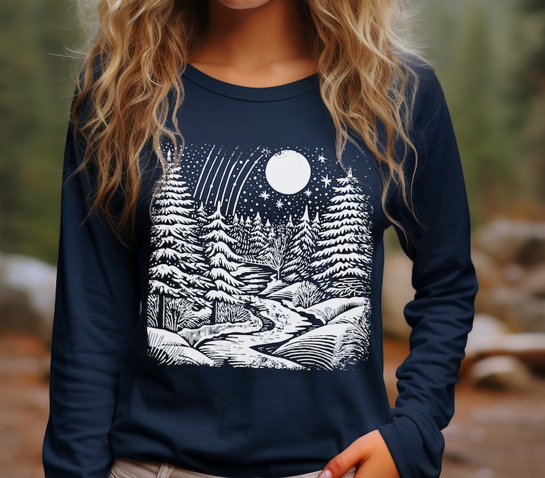 Peut inclure: Un t-shirt &agrave; manches longues bleu marine avec un imprim&eacute; graphique blanc repr&eacute;sentant une sc&egrave;ne de for&ecirc;t enneig&eacute;e avec une pleine lune et des &eacute;toiles filantes.