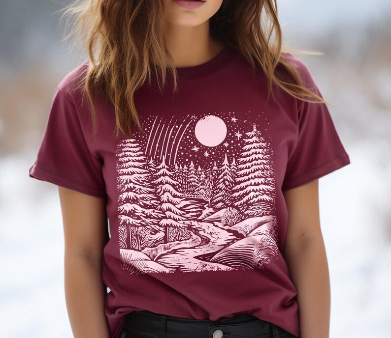 May include: A maroon t-shirt with a pink graphic print of a snowy forest scene with a full moon and shooting stars.