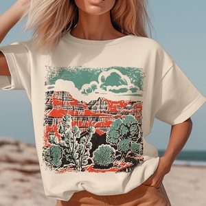 May include: A cream-colored t-shirt with a vintage-style graphic print of a red mountain range with green trees and a blue cloud.