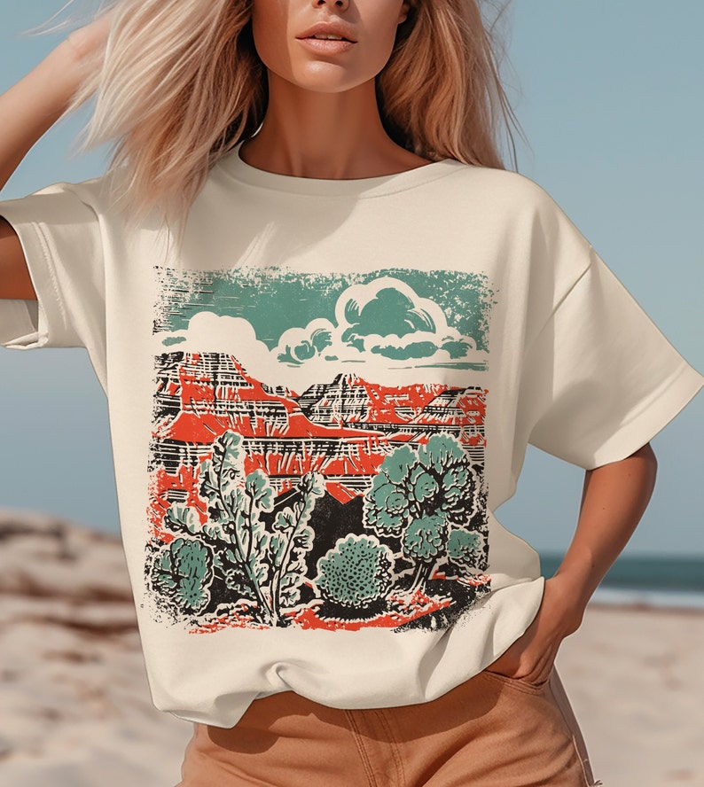 May include: A cream-colored t-shirt with a vintage-style graphic print of a red mountain range with green trees and a blue cloud.