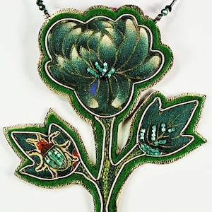 Può includere: Una collana con pendente floreale fatto a mano con un design verde scuro e oro. Il pendente presenta un grande fiore e foglie con dettagli di insetti, il tutto delineato in oro. La collana è appesa a un cordino nero.