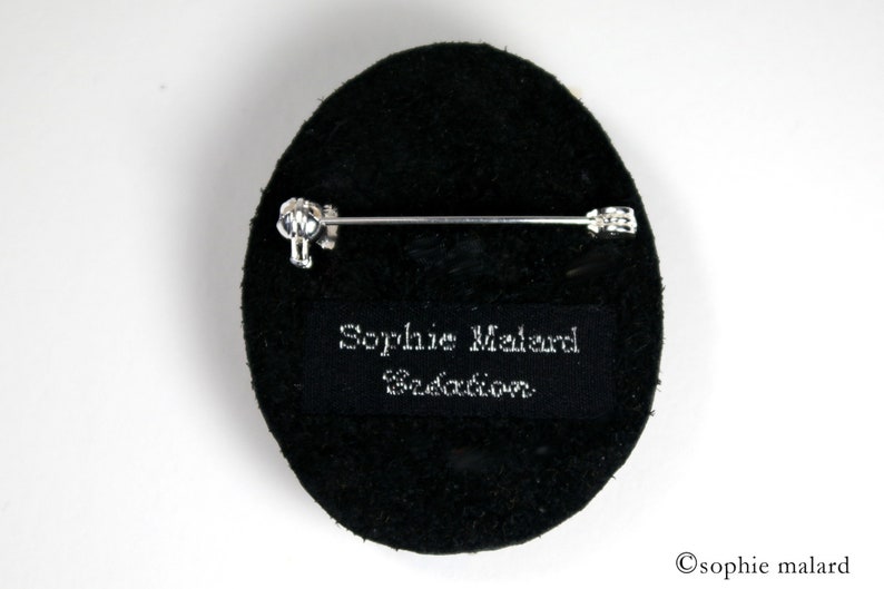 Puede incluir: Broche ovalada negra con un alfiler plateado y una etiqueta negra que dice "Sophie Malard Creation".