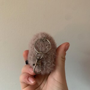 May include: A fluffy, light pink pom-pom keychain with a silver metal ring and a silver metal clasp.