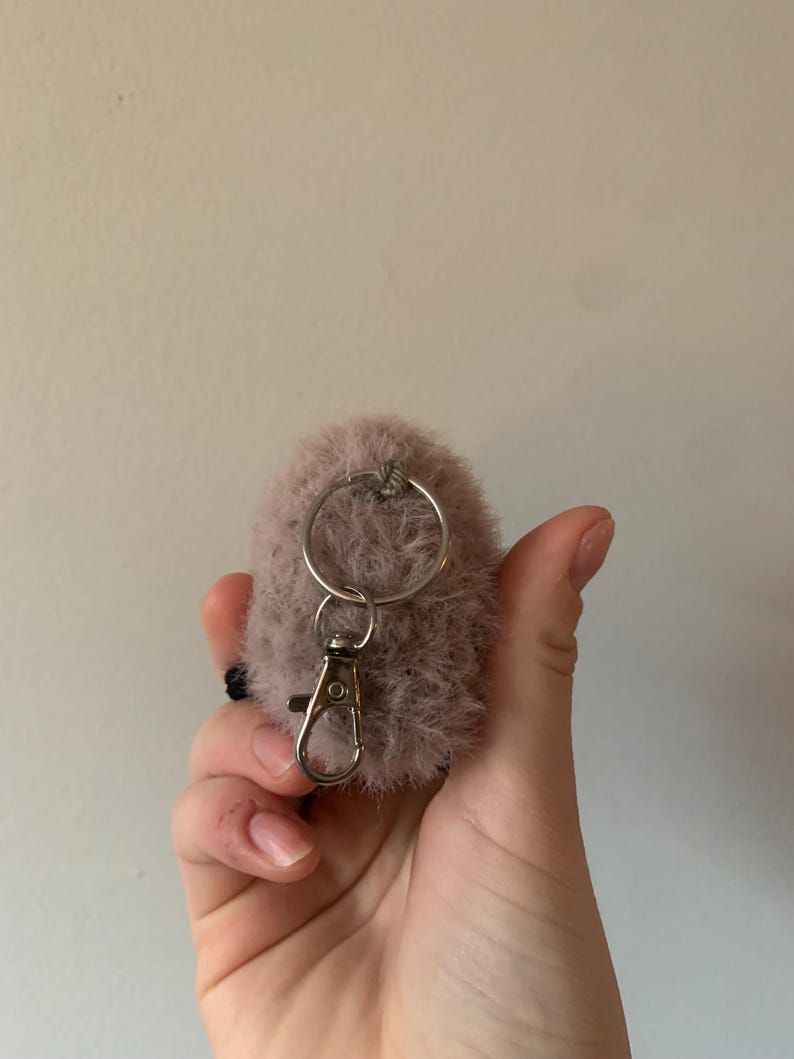 May include: A fluffy, light pink pom-pom keychain with a silver metal ring and a silver metal clasp.