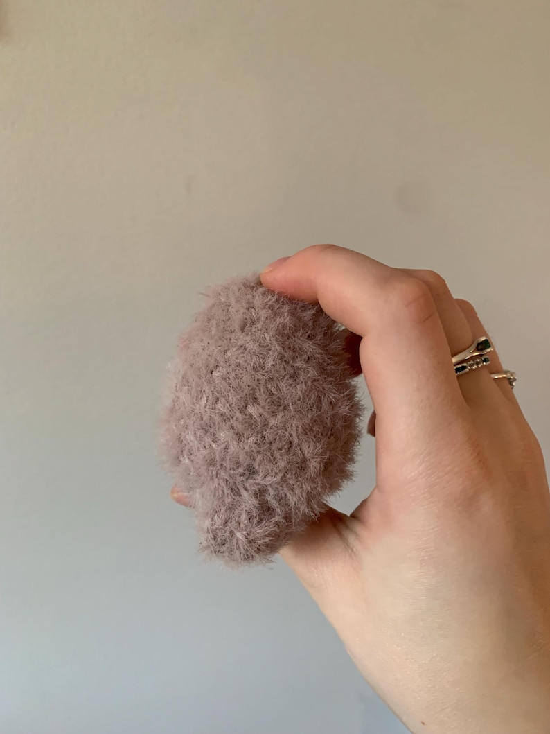 May include: A soft, fluffy, light pink makeup brush. The brush is held in a hand.