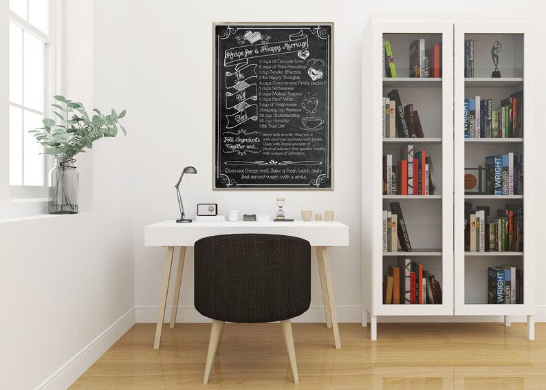 May include: A black chalkboard with a white inscription that reads "Recipe for a Happy Marriage". The inscription lists ingredients for a happy marriage, such as "1 cup of Genuine Love", "1 cup of Tender Affection", and "1 cup of True Commitment". The chalkboard is framed in a light wood frame and is hanging on a white wall in a home office.