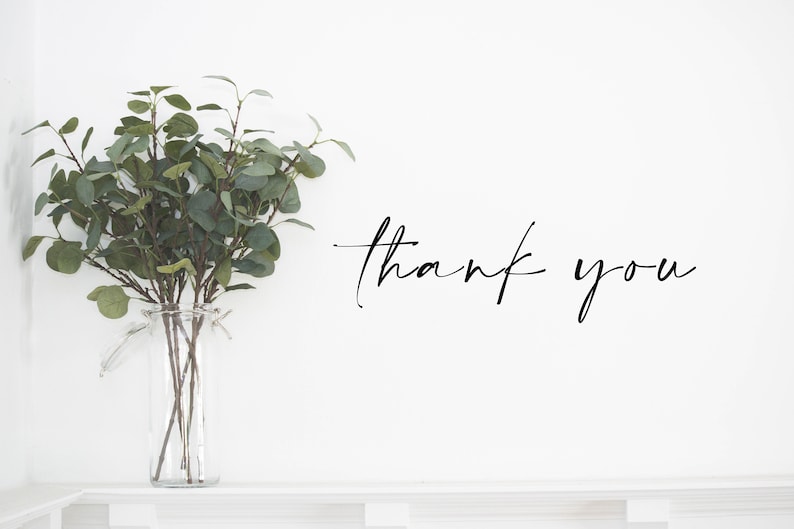 May include: A clear glass vase holds green eucalyptus branches. The words "thank you" are written in elegant black script on a white background. The vase sits on a white shelf.