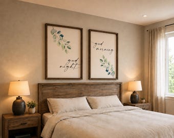 Può includere: Due quadri rettangolari con cornici in legno scuro che presentano illustrazioni di foglie di eucalipto verdi su sfondo bianco. Il pezzo a sinistra riporta la scritta "good night" e quello a destra "good morning" in corsivo nero.