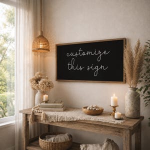 Może przedstawiać: Prostokątny szyld ścienny z czarnym tłem i cienką drewnianą ramą, zawierający biały kursywny napis "customize this sign" wyśrodkowany na powierzchni. Szyld jest zamontowany na ścianie nad drewnianym stolikiem konsolowym.
