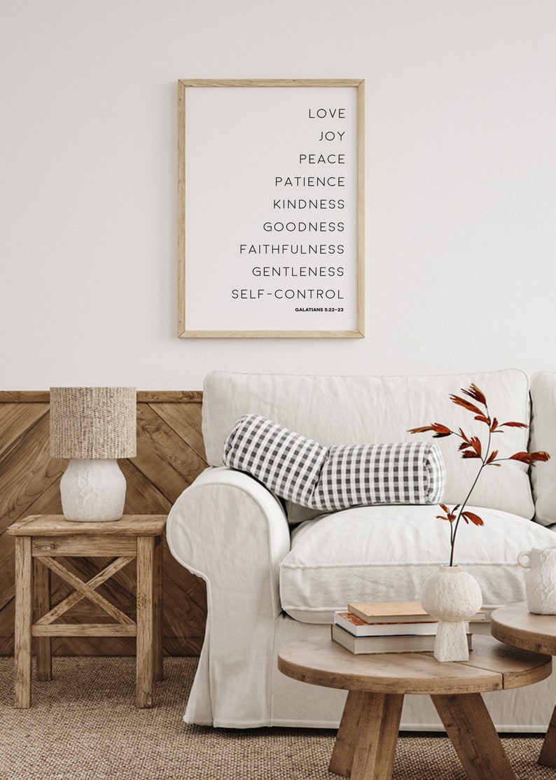 May include: A framed print with the words "Love, Joy, Peace, Patience, Kindness, Goodness, Faithfulness, Gentleness, Self-Control" in black text. A white sofa with a black and white checkered bolster pillow is in front of a wooden wall.