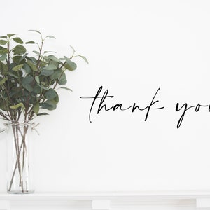 May include: A white wall with a vase of green eucalyptus branches and the text "thank you" written in black cursive.
