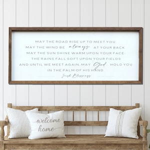 May include: A wooden sign with a white background and black text. The sign reads "May the road rise up to meet you. May the wind be always at your back. May the sun shine warm upon your face. The rains fall soft upon your fields and until we meet again. May God hold you in the palm of his hand. Irish Blessings."