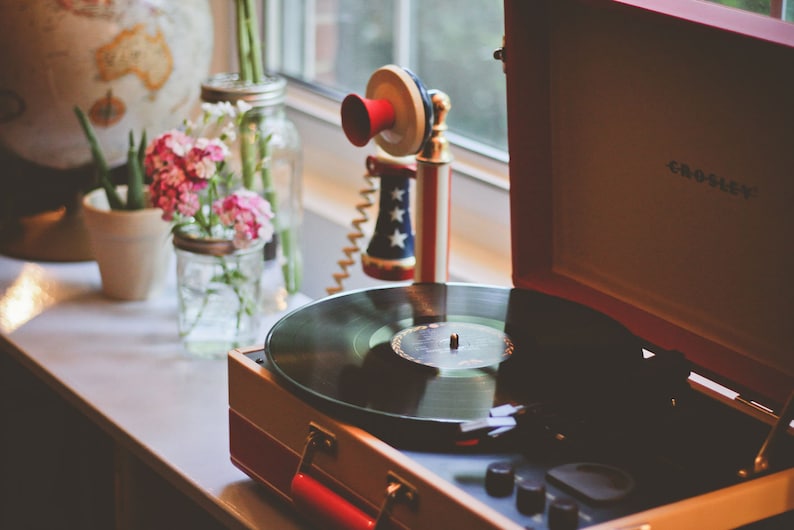May include: A vintage-style red and white record player with a black vinyl record on the turntable. The record player is open and the lid is propped up. There is a red, white, and blue toy telephone on the table next to the record player.