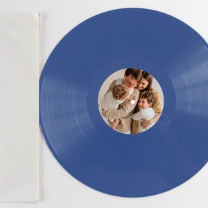 May include: A blue vinyl record with a photo of a family of four. The photo shows a man, a woman, and two children. The man is holding the younger child, and the woman is holding the older child. The photo is in a circular frame in the center of the record.