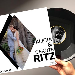 May include: A white record album cover with black diamond shapes. The cover features a photo of a couple in a wedding setting. The text on the cover reads "Alicia & Dakota Ritz" and "EST. 10.6.19".