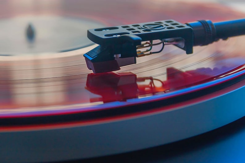 May include: A close-up of a red vinyl record spinning on a turntable. The needle is in the groove, and the record is reflecting the light.